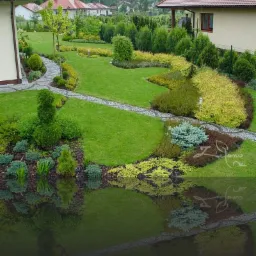 Rozległy, zadbany ogród z krętymi ścieżkami z kostki, formowanymi krzewami i rabatami z różnorodnych roślin, widok z góry na starannie zaprojektowany teren.